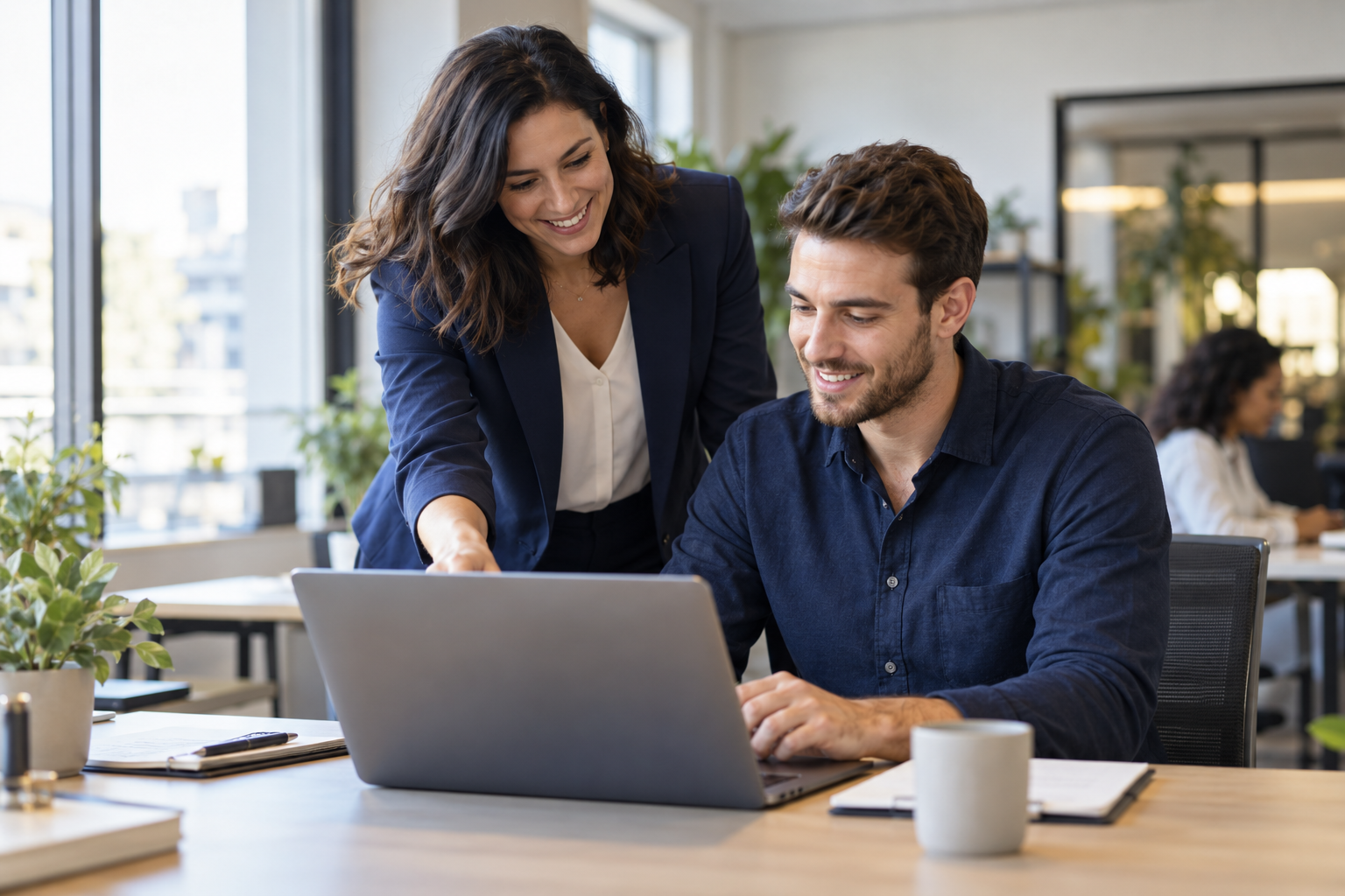 A smiling manager helping an employee at a laptop
